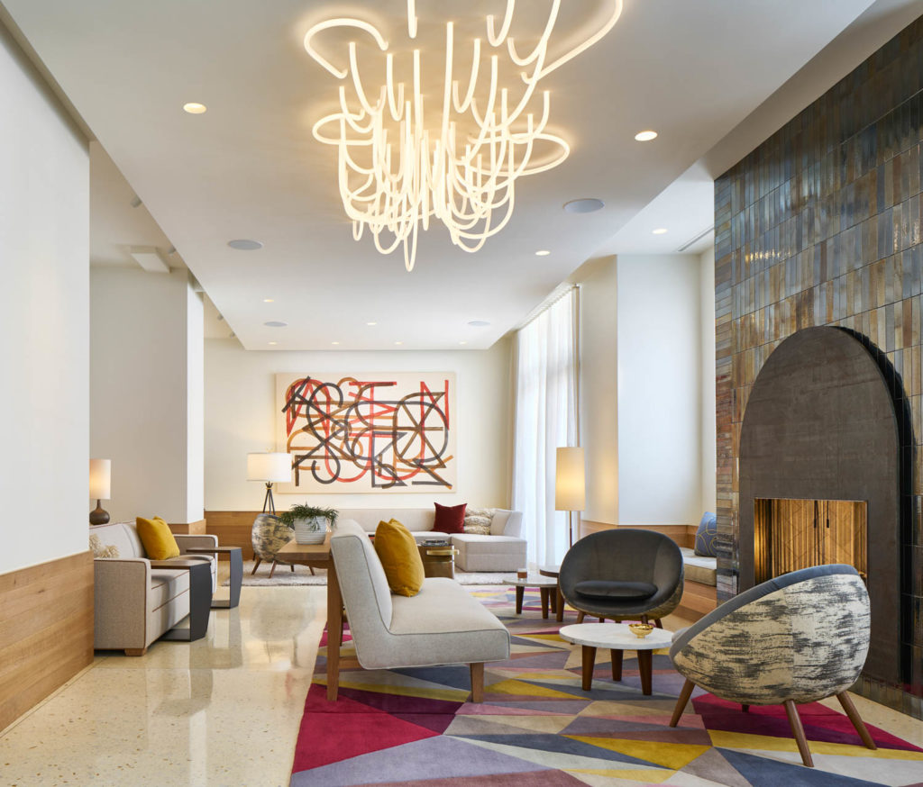 The James Hotel by Dufner Heighes, lobby lounge with a sculptural light fixture, colorful rug and fireplace, Chicago