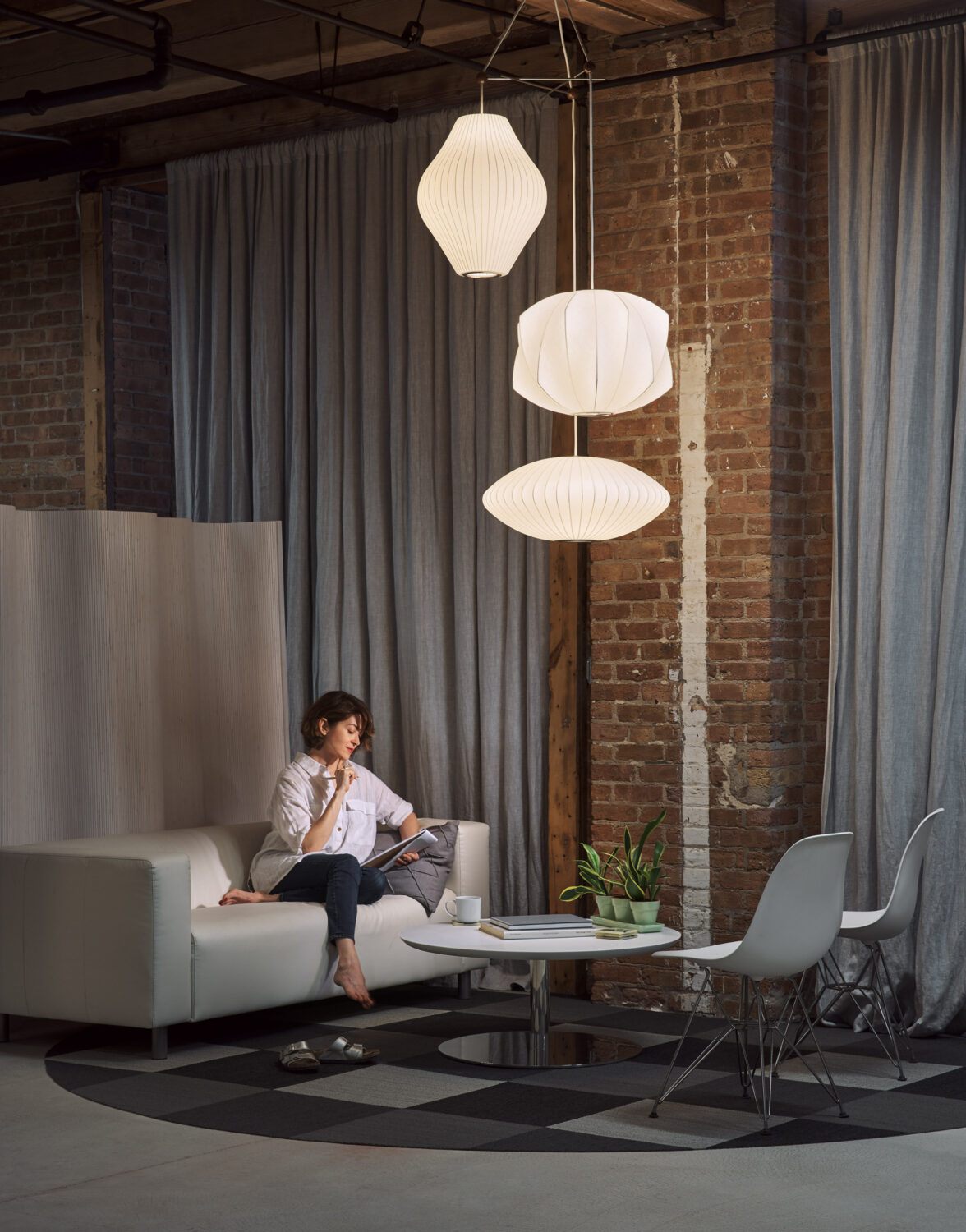 Woman reading on a white sofa beneath paper bubble pendant lamps in Christopher Barrett's brick-walled Chicago studio