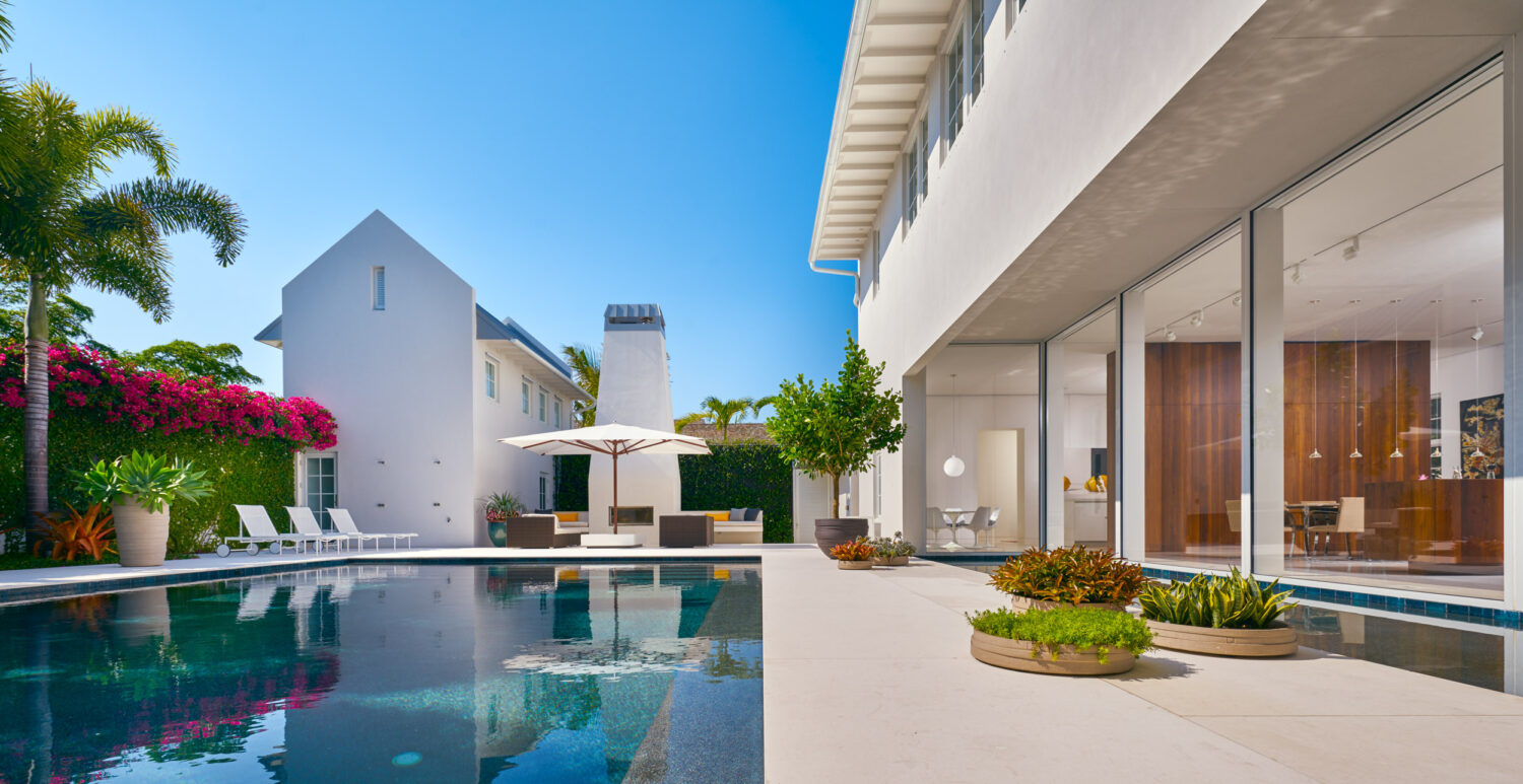 Pool and terrace of the Podesta Residence, with a white gabled guest wing, outdoor fireplace and bougainvillea