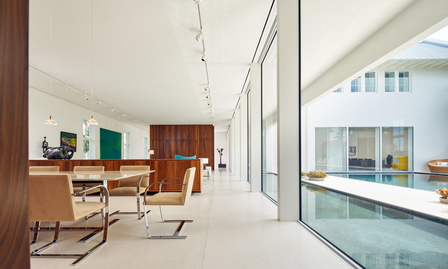 Dining area and gallery-like living space along full-height glass facing the courtyard pool