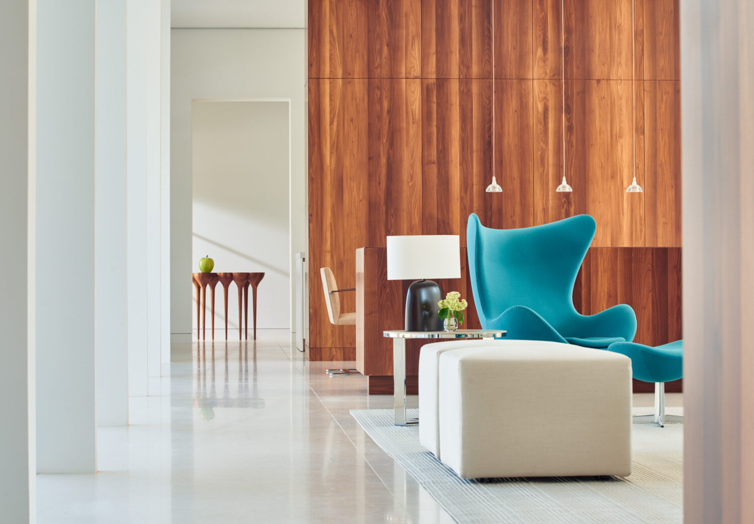 Turquoise Egg chair and ottomans before a walnut-paneled wall, with a sculptural console beyond
