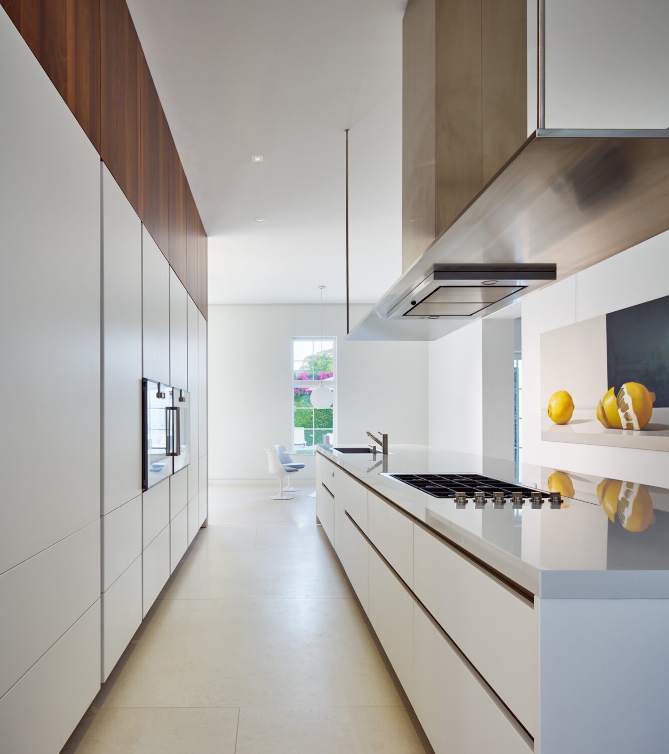 Long white kitchen with walnut upper cabinets and a stainless steel hood