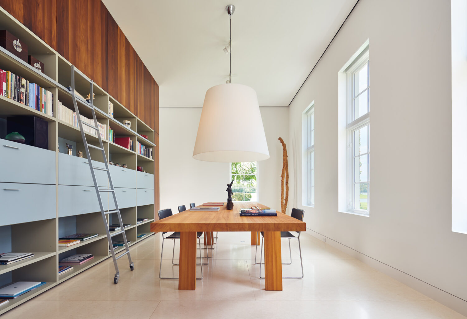 Library with floor-to-ceiling shelving, rolling ladder and an oversized pendant above a wood table
