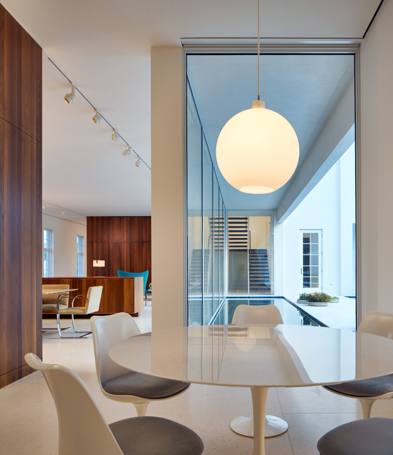 Breakfast table beneath a globe pendant, with a glass wall looking onto the stair and courtyard