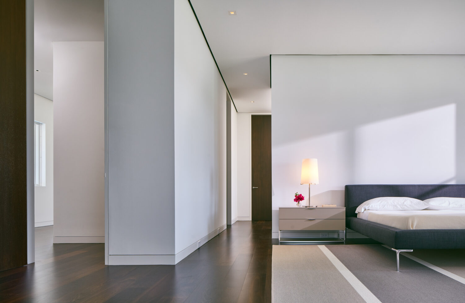 Primary bedroom with white partition walls and dark wood floors in afternoon light