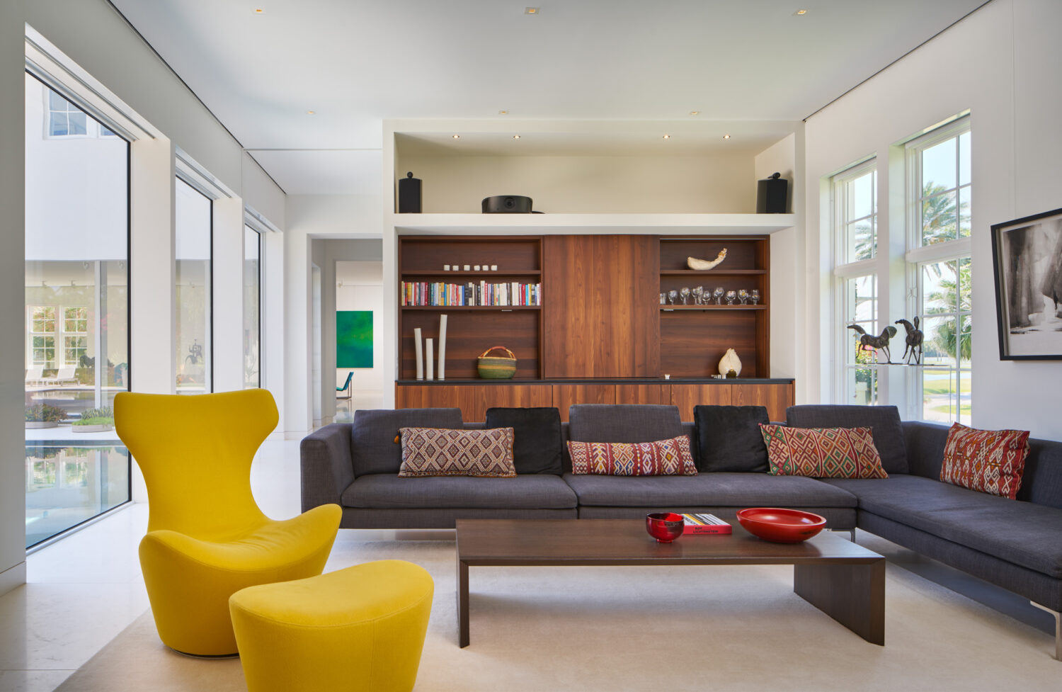 Family room with a yellow lounge chair, charcoal sectional and walnut media wall