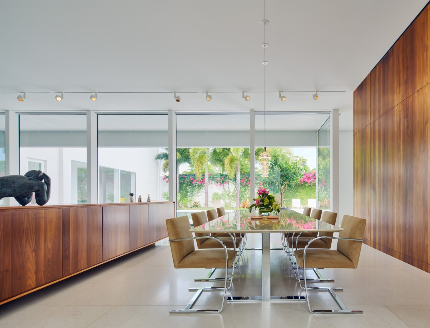 Dining room with walnut credenza and Brno chairs, facing the garden through full-height glass