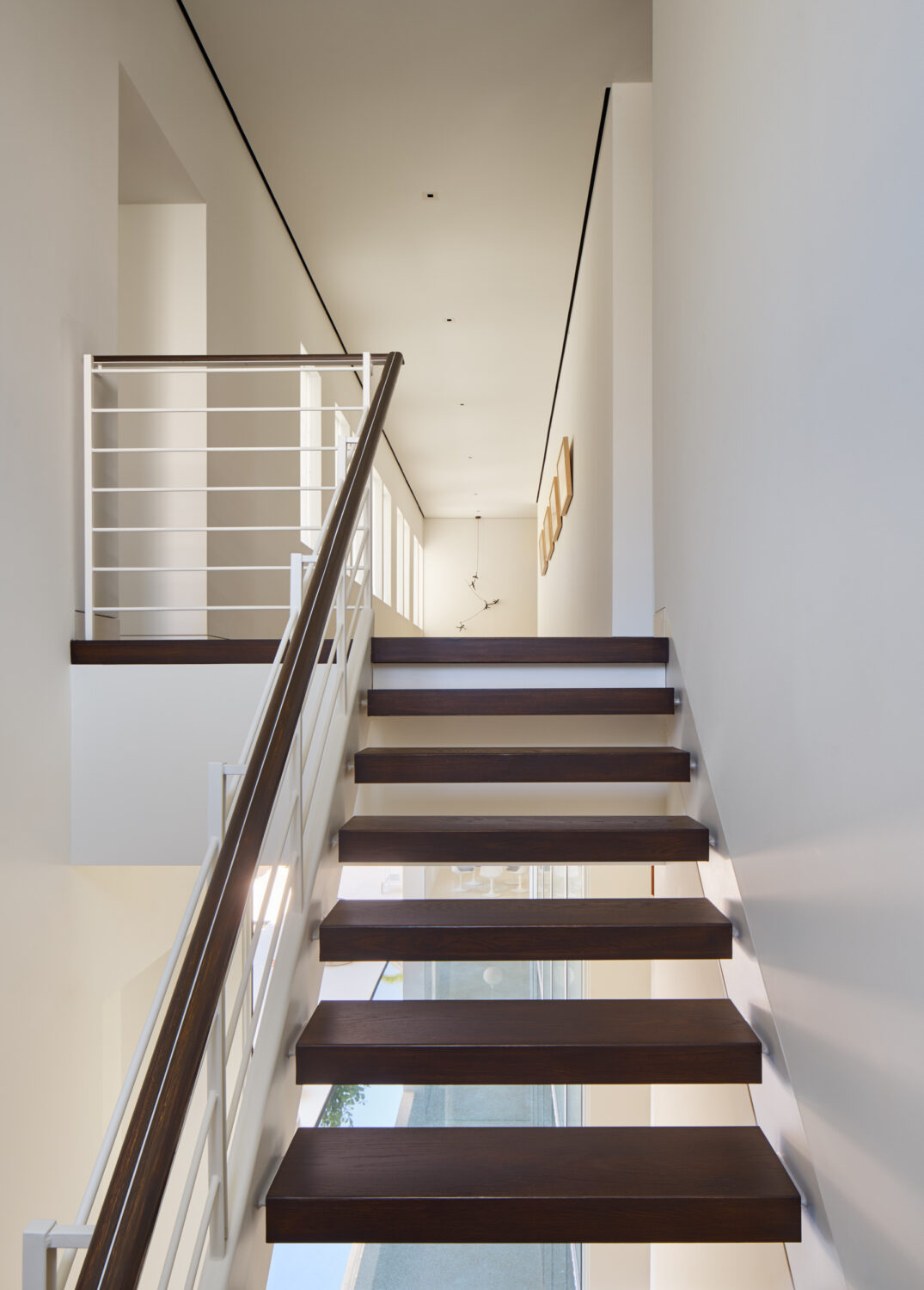 Floating dark wood stair with a white railing rising to the upper hall