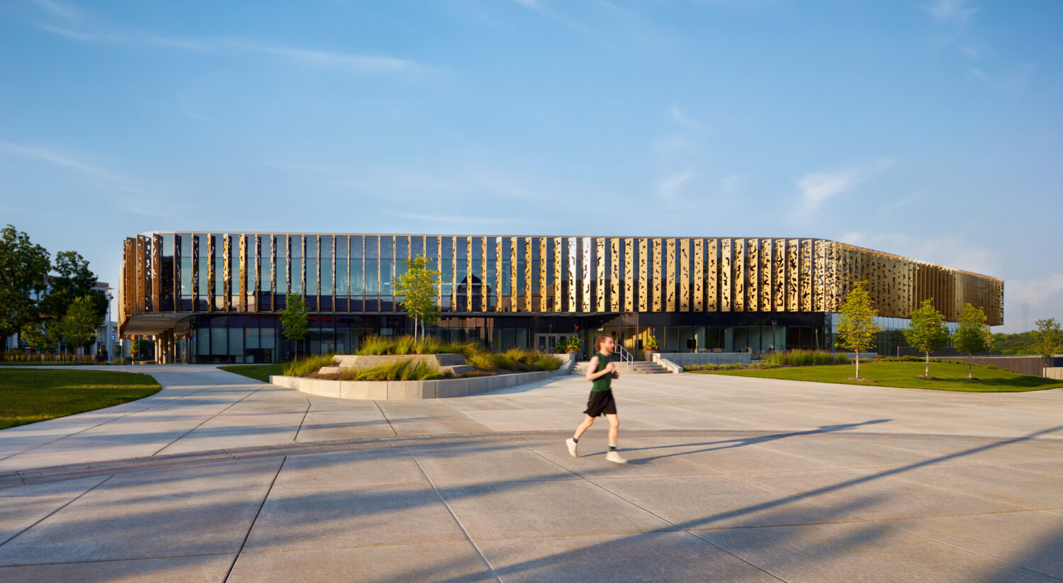 Long facade of the Western Michigan University Student Center with gold fins in late-day light as a runner crosses the plaza