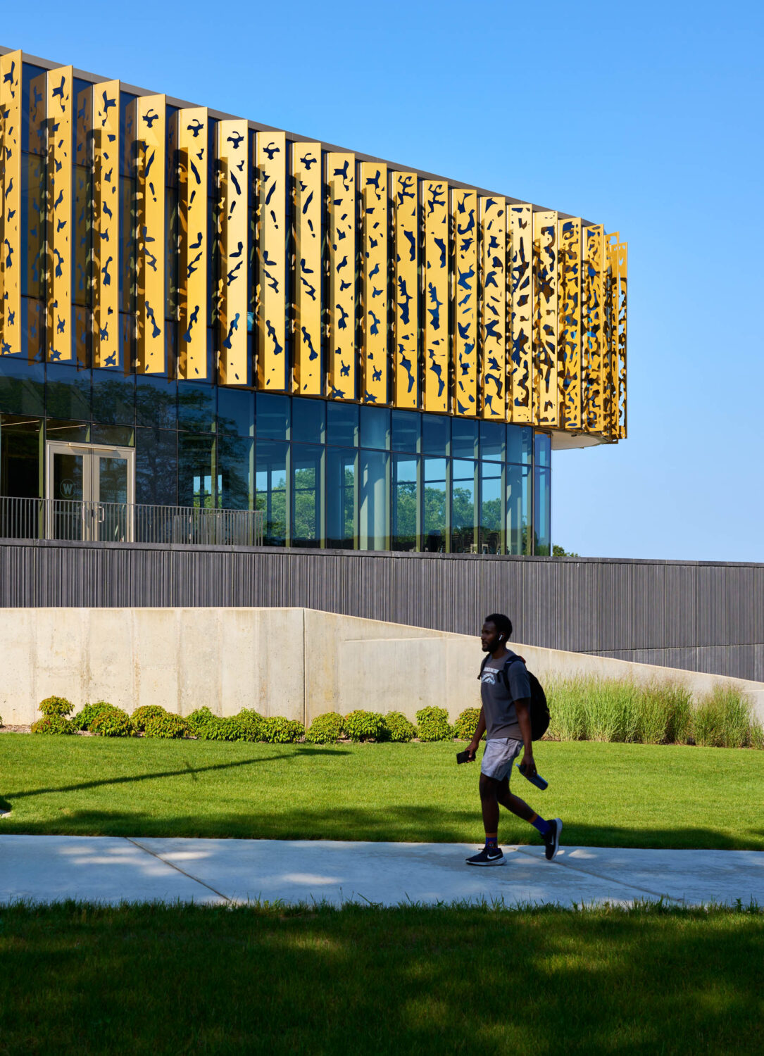 Student walking past the Western Michigan University Student Center, its gold fins cantilevered above a concrete wall and lawn
