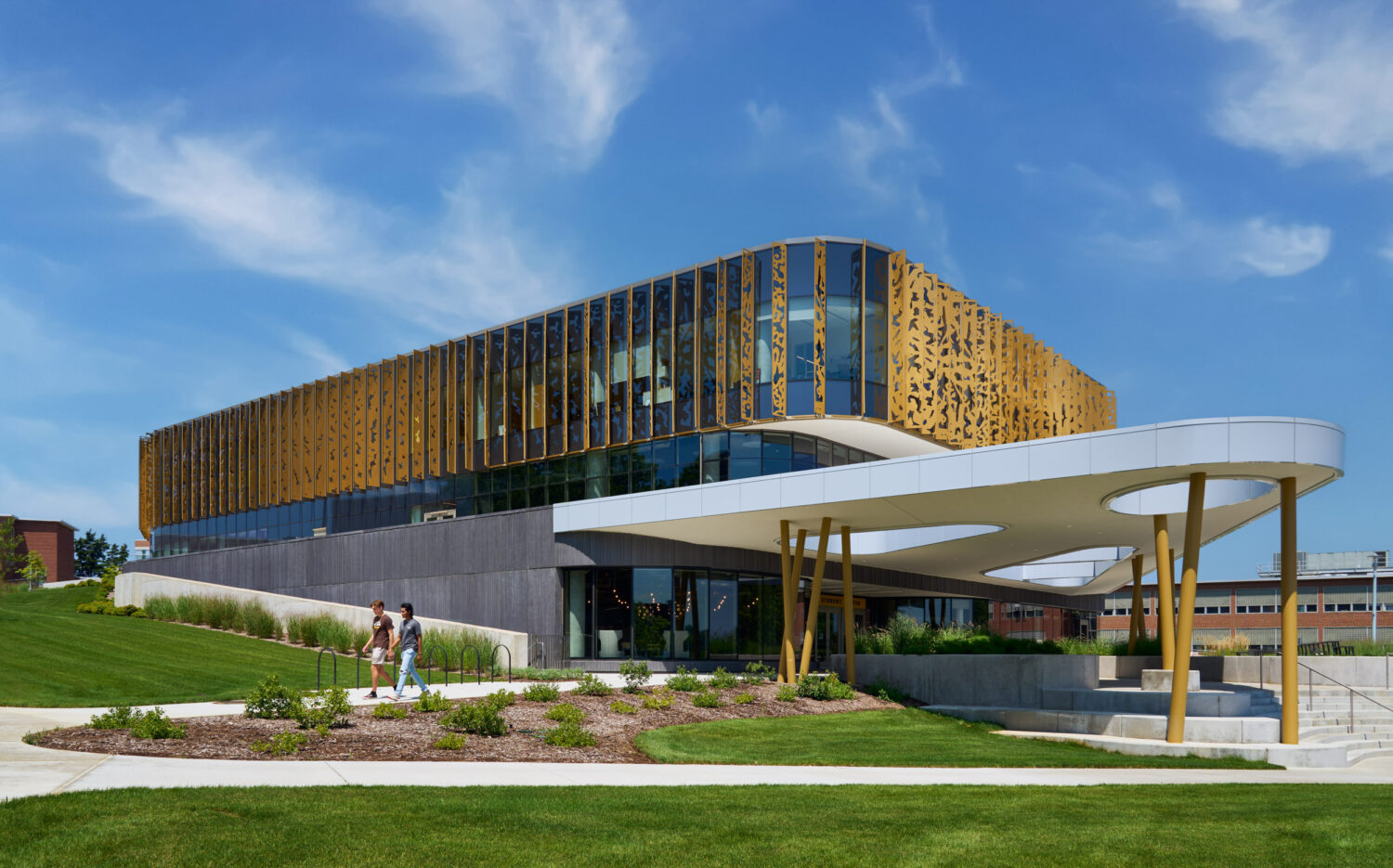 Western Michigan University Student Center with its white curved canopy on gold columns, students walking along the landscaped path