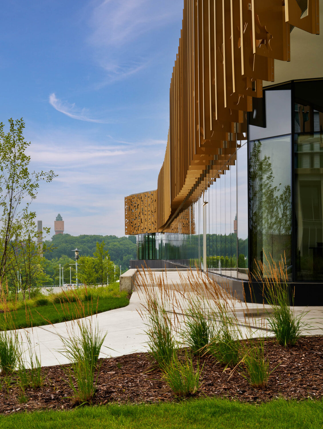 Gold fins of the Western Michigan University Student Center cascading overhead beside the glass wall, with tall grasses in the foreground