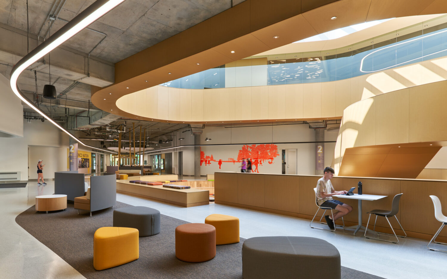 Lounge seating in bright colors beneath the curved cedar balcony of the Western Michigan University Student Center atrium