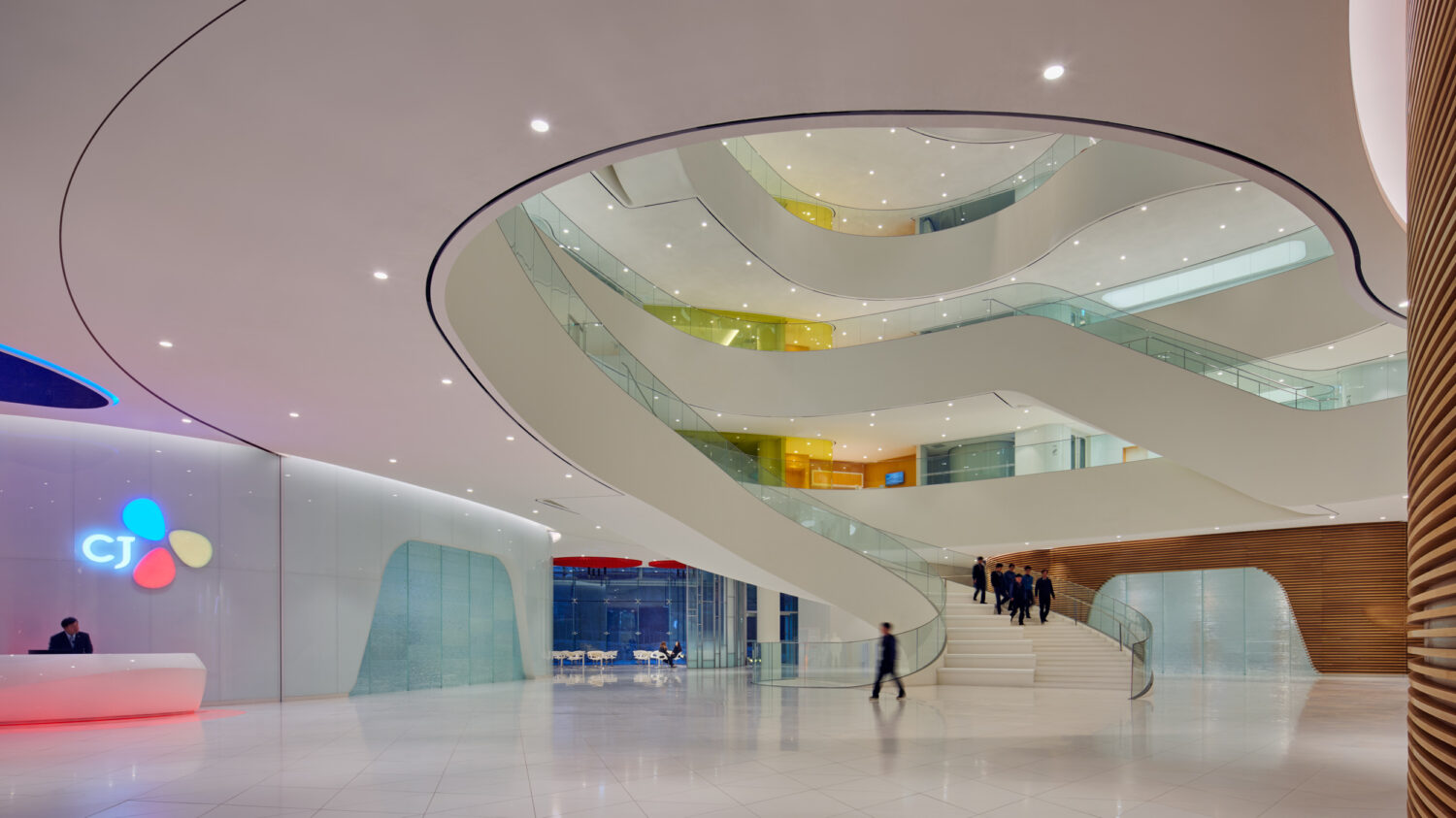 CJ Blossom Park lobby with the illuminated CJ logo, reception desk and a sweeping white stair rising through an oval opening in the ceiling