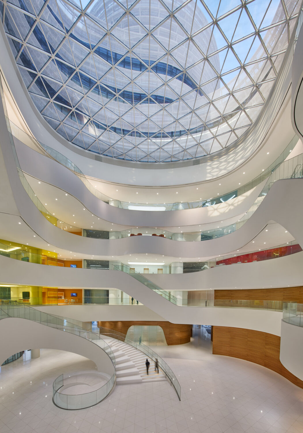 Multi-story atrium at CJ Blossom Park beneath a triangulated glass skylight, with curving white balconies and a spiral stair
