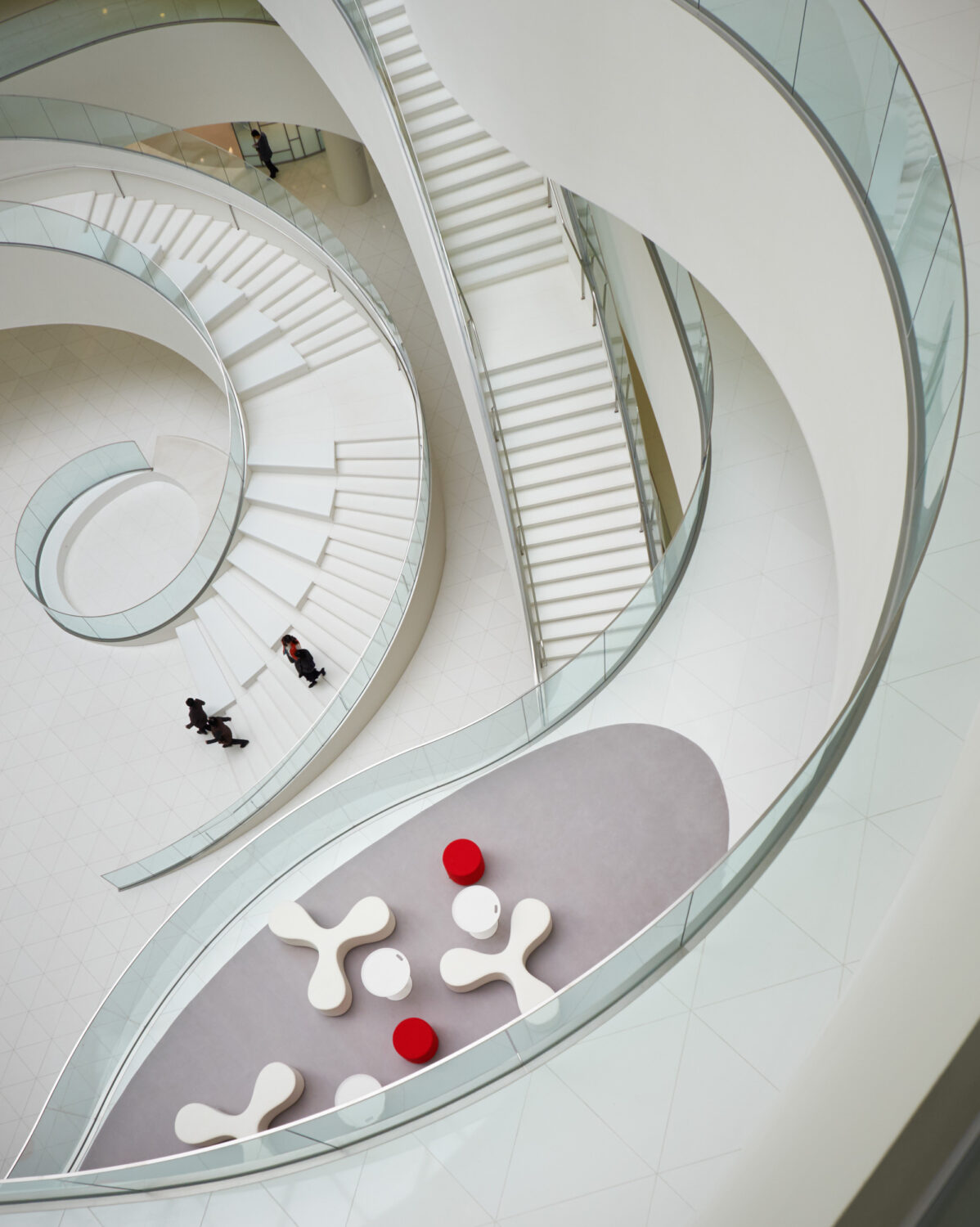 Looking down on spiraling white stairs and glass railings in the CJ Blossom Park atrium, with red and white lounge seating below