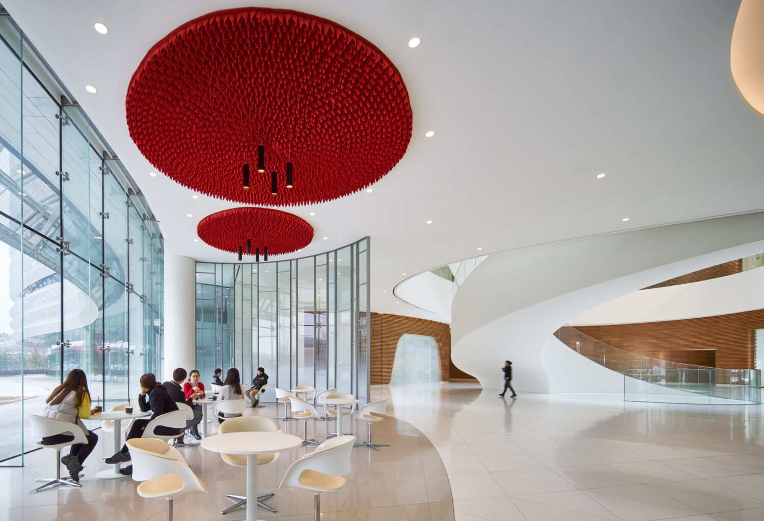 Ground floor café at CJ Blossom Park with red ceiling sculptures over white tables, glass walls and a curving white stair