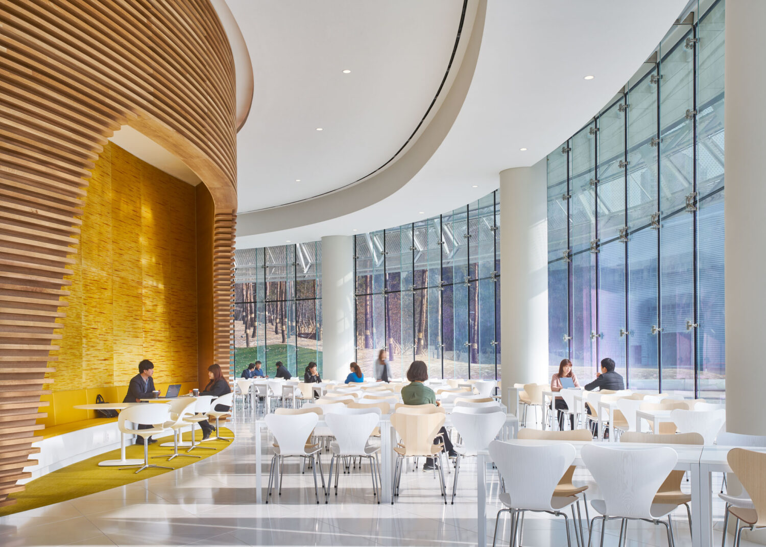 Employee dining hall at CJ Blossom Park with a yellow banquette under a curved wood slat wall and floor-to-ceiling glass