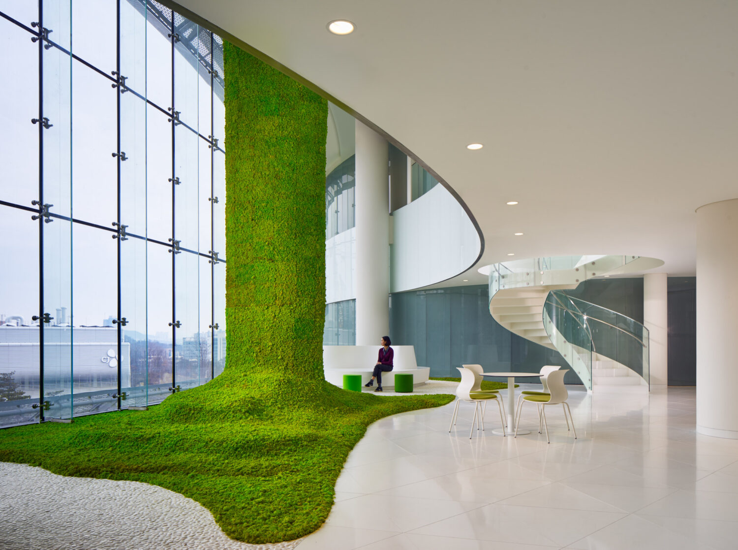 Living forest at CJ Blossom Park, a moss-covered column spreading across the floor beside tall windows and a spiral stair