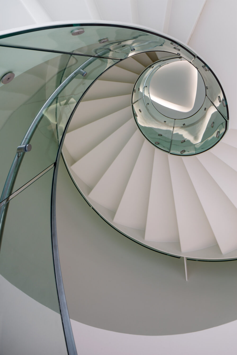 Looking up into a white spiral stair with a green glass railing at CJ Blossom Park