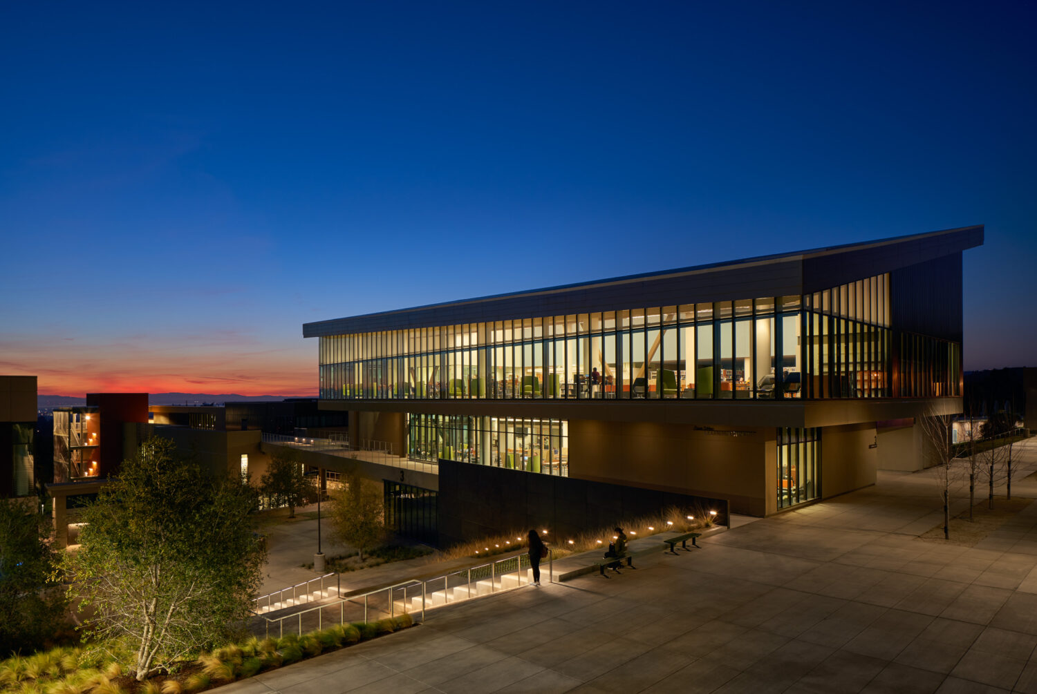 Ohlone College academic building by CannonDesign at dusk, glowing glass above a landscaped slope