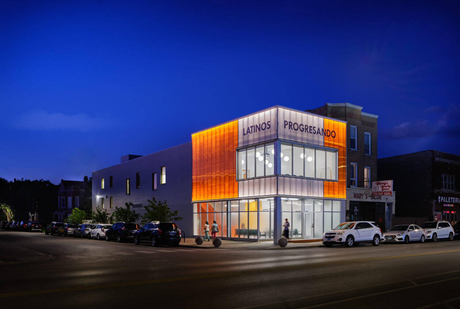 Latinos Progresando community center by Canopy at dusk, orange-lit facade under a deep blue sky, Chicago