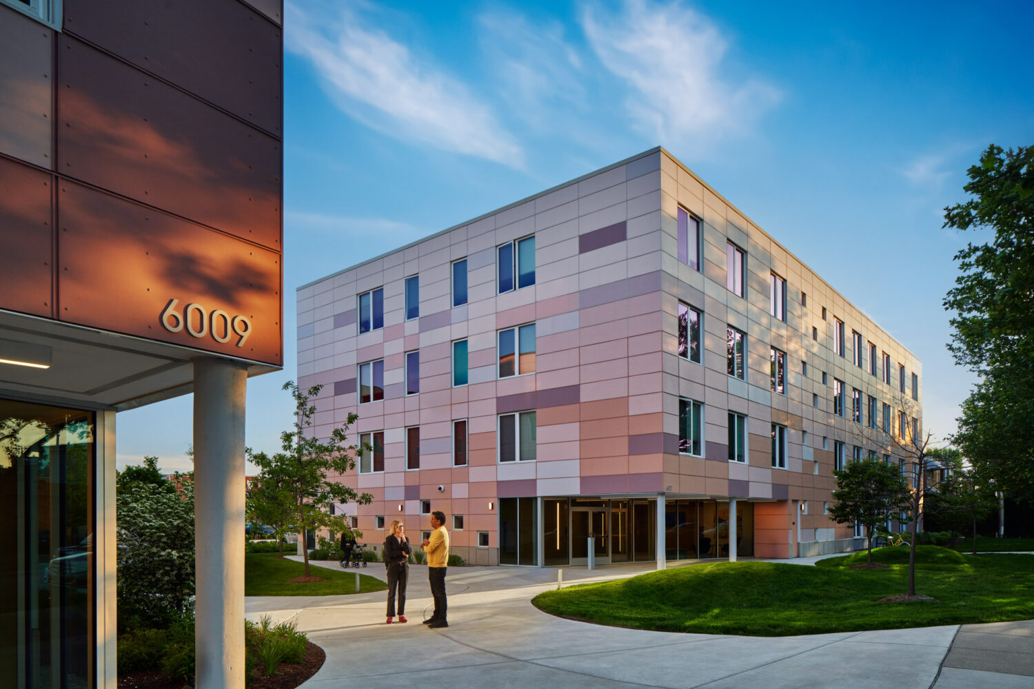 Lawrence and Austin apartments by Canopy in late-day light, pale brick facade and entry sign, Chicago