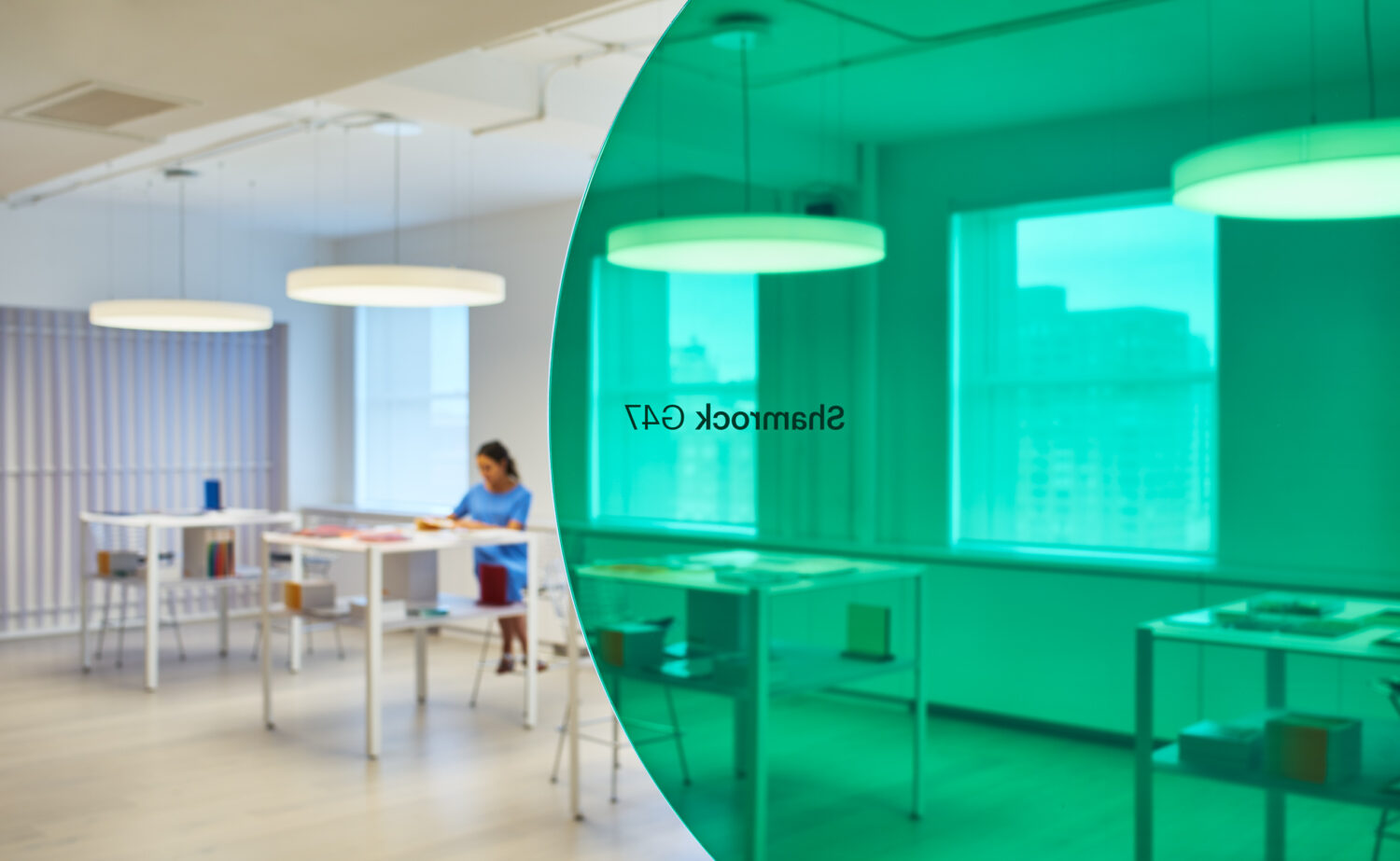 Glowing green curved glass wall beside white work tables and pendant lights in the 3form showroom