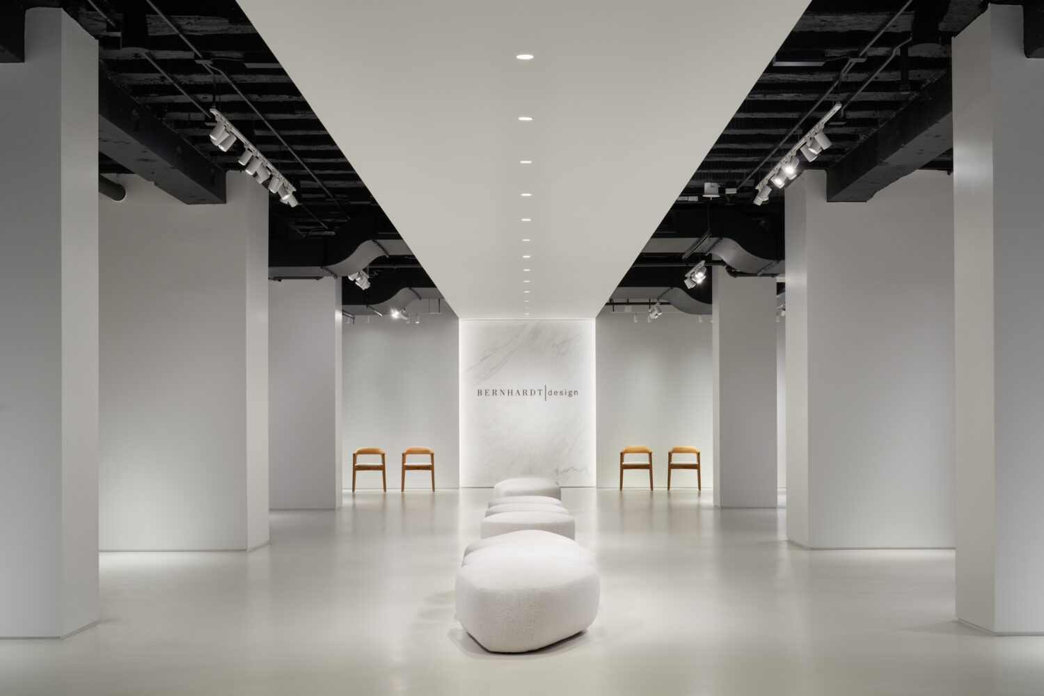 Long white Bernhardt showroom gallery with a sculptural white seat on the center axis under a black open ceiling