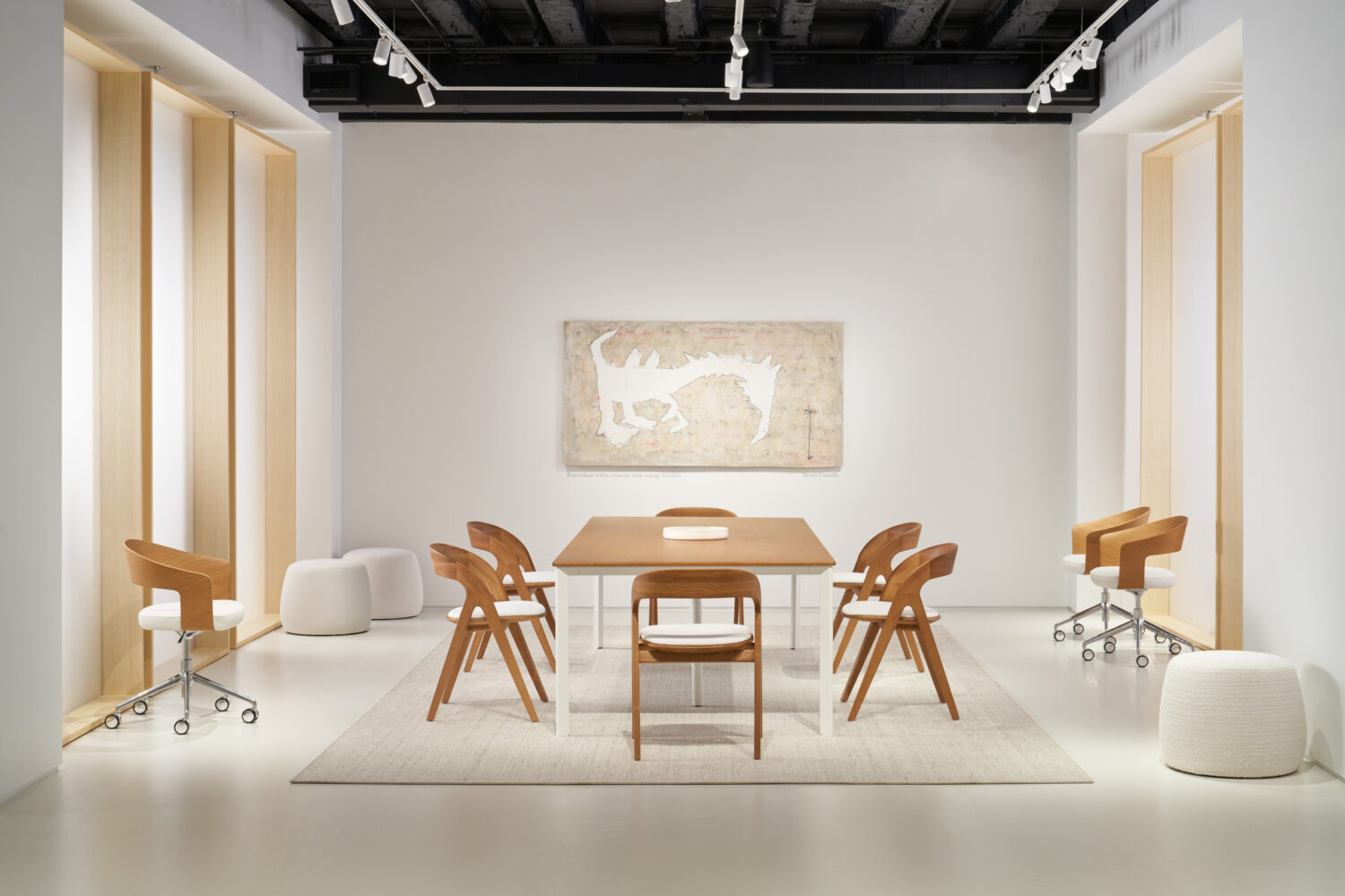 Wood dining table with sculptural chairs and white pouf seats framed by pale wood panels in the Bernhardt showroom