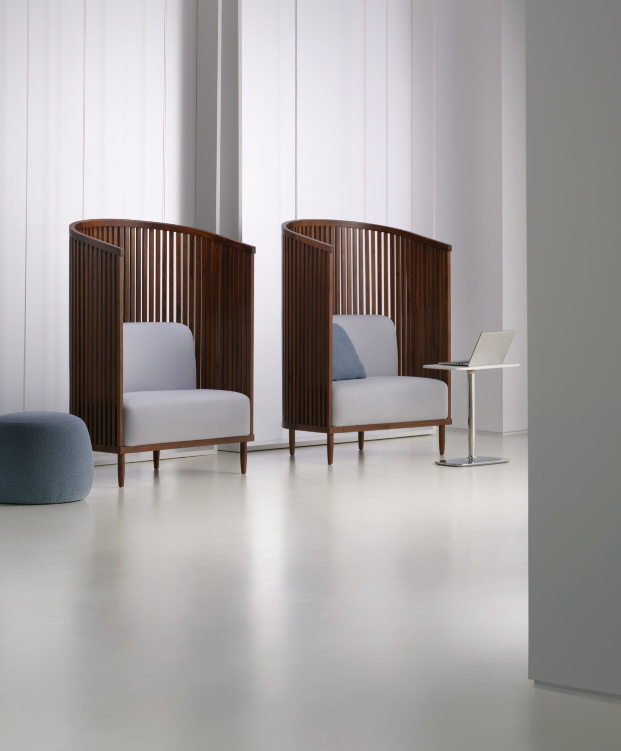 Pair of slatted wood high-back lounge chairs with gray cushions in a bright white Bernhardt showroom