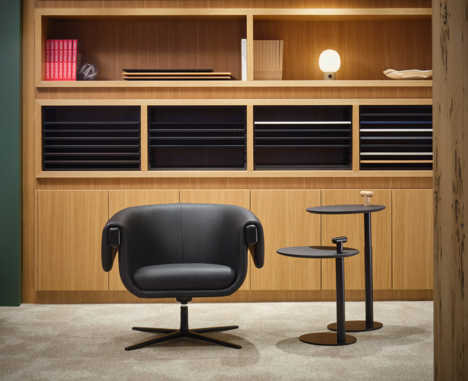 Black leather lounge chair and side table before oak shelving in the Bulo showroom