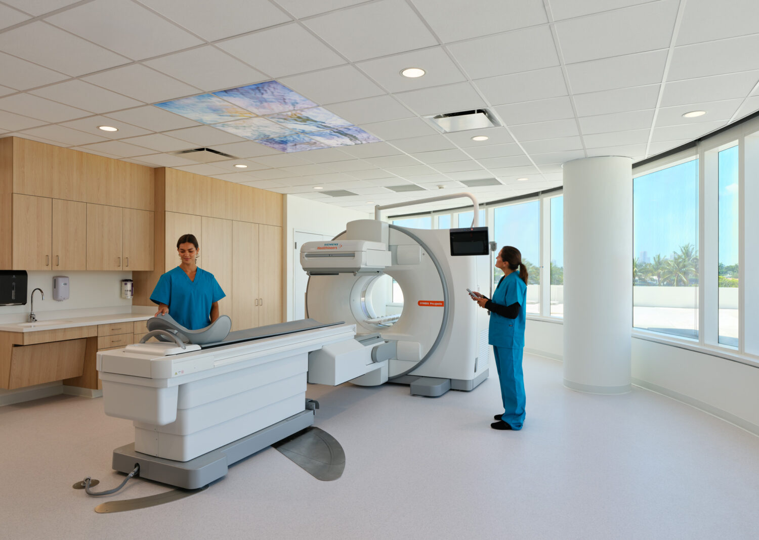 CT imaging room with care team beside bay windows, Braman Comprehensive Cancer Center by CannonDesign, Miami Beach, Florida