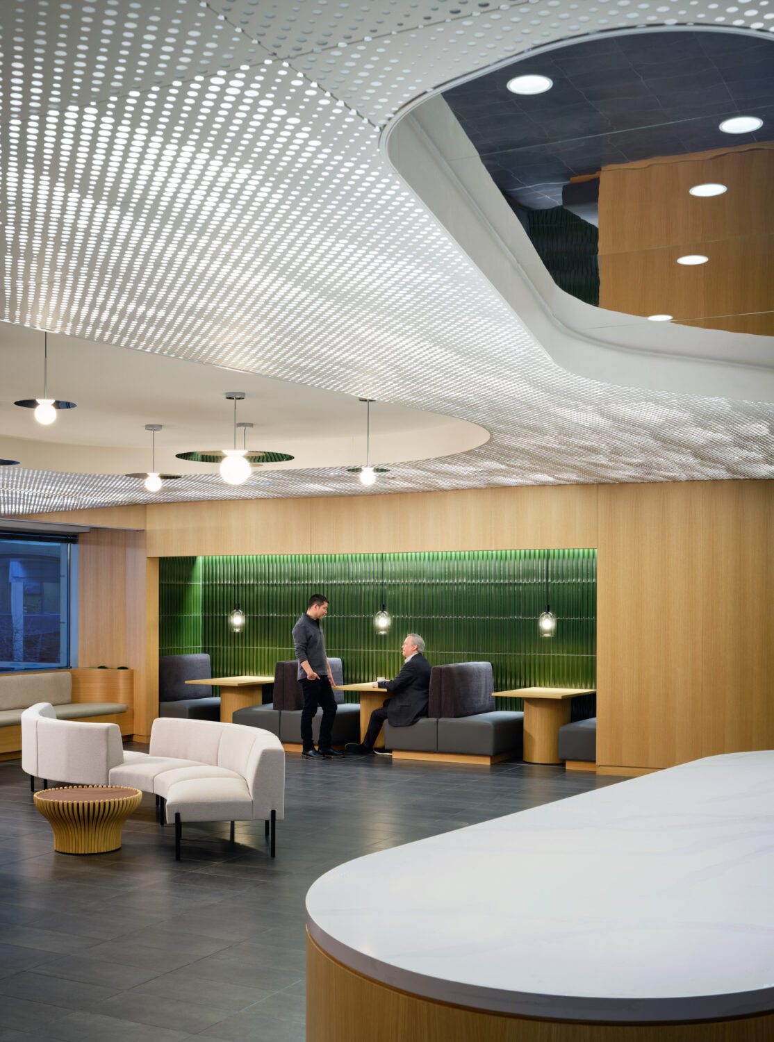 Lounge with a curved white counter, soft seating and a green moss wall under a sculpted ceiling at the Northwestern Medicine Faculty Office Center