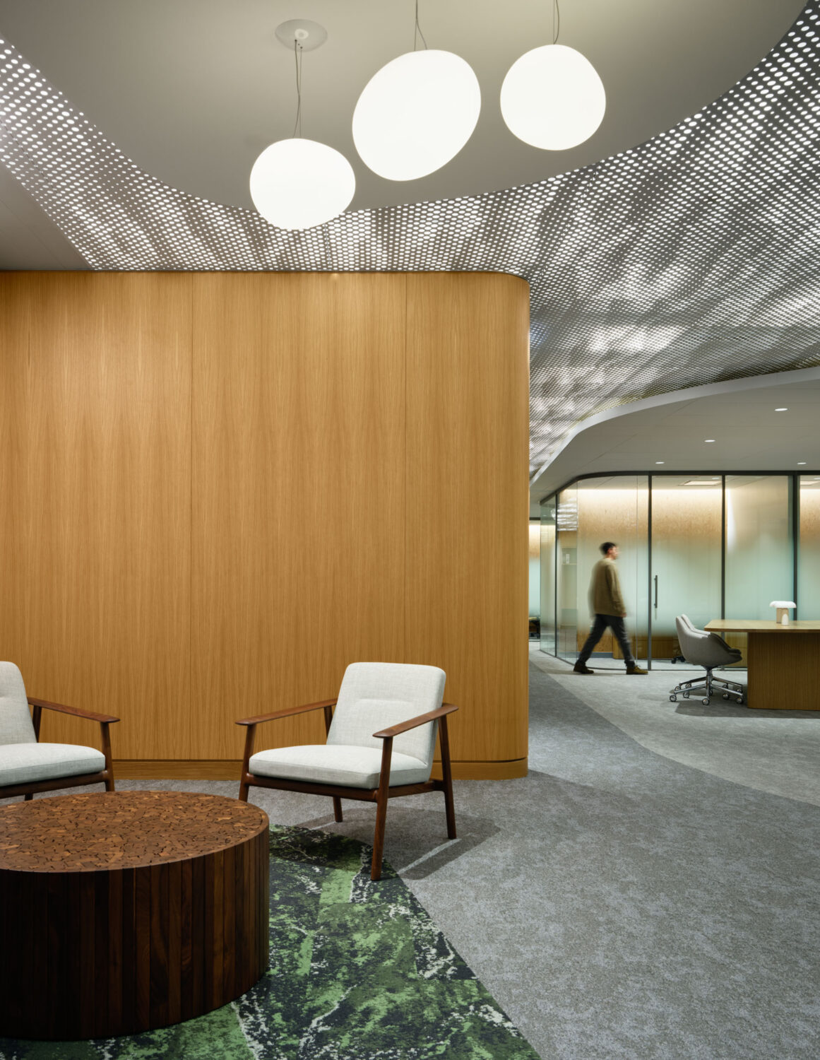 Pair of armchairs and a round table beneath globe pendants beside an oak-clad wall at the Northwestern Medicine Faculty Office Center