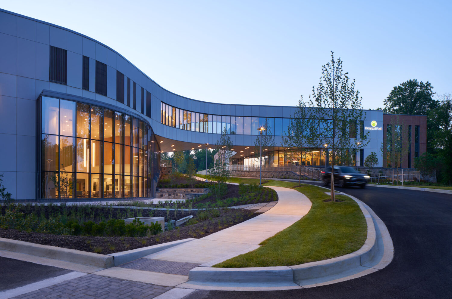 Main entrance at dusk with a curving glass facade and entry drive, Sheppard Pratt Baltimore/Washington Campus by CannonDesign, Elkridge, Maryland