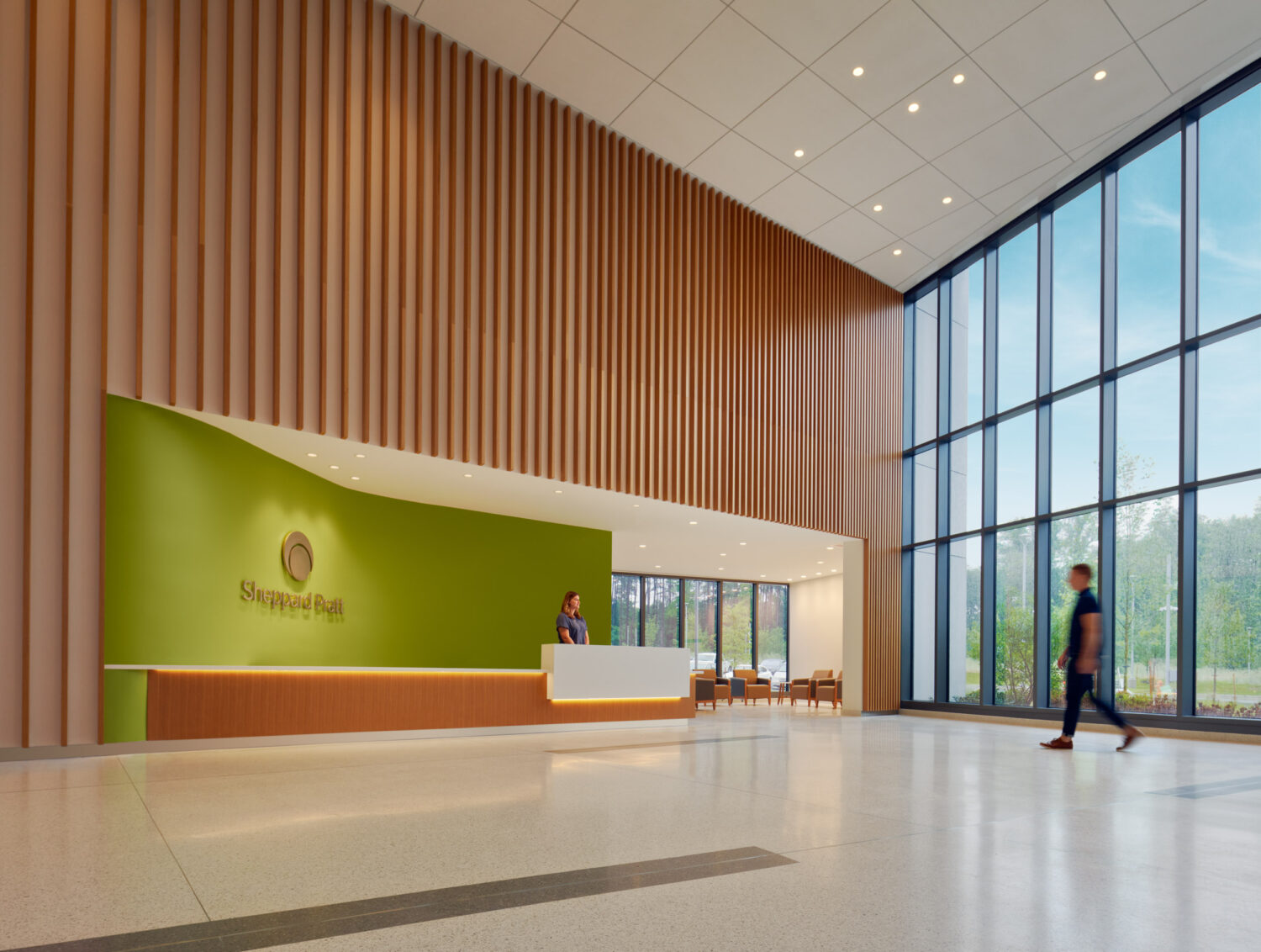 Double-height lobby with a green reception wall and wood slats, Sheppard Pratt Baltimore/Washington Campus by CannonDesign, Elkridge, Maryland