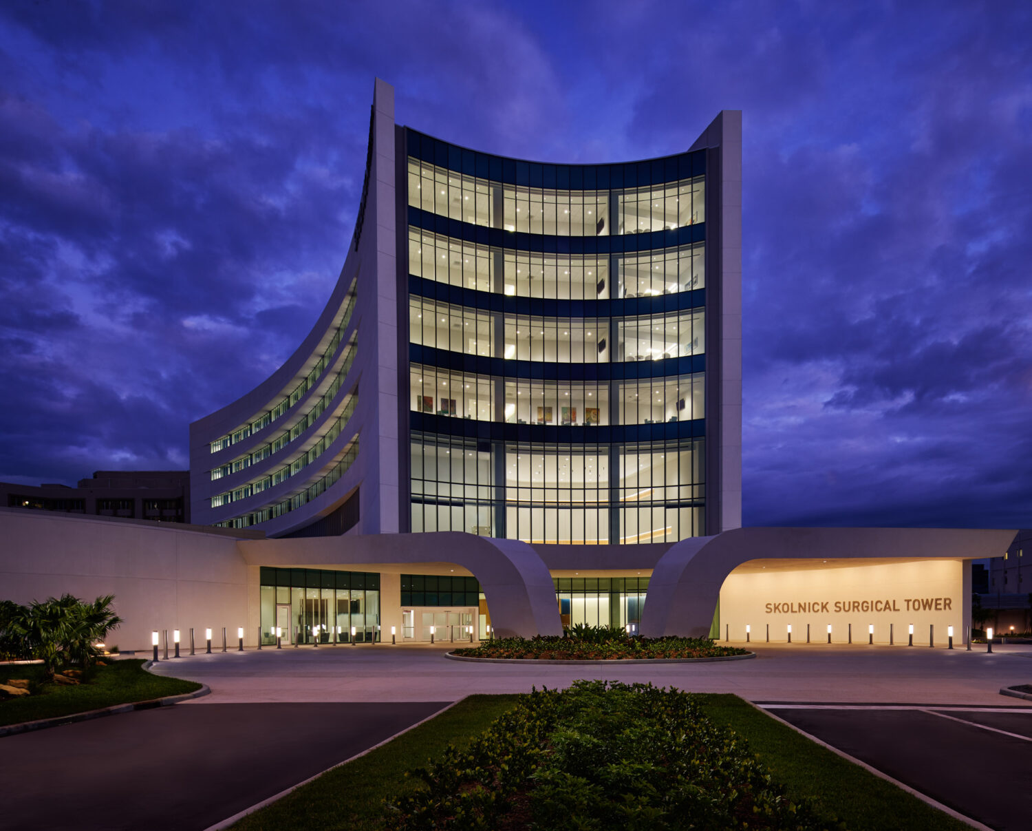 Exterior at dusk with the curved tower and lit entrance, Skolnick Surgical Tower by CannonDesign, Miami Beach, Florida