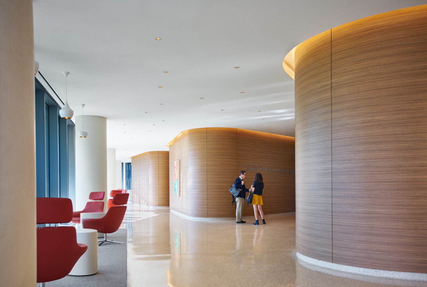 Curved wood-clad walls and red lounge chairs along a window wall, Jacobs Medical Center, UC San Diego Health by Yazdani Studio of CannonDesign, La Jolla, California