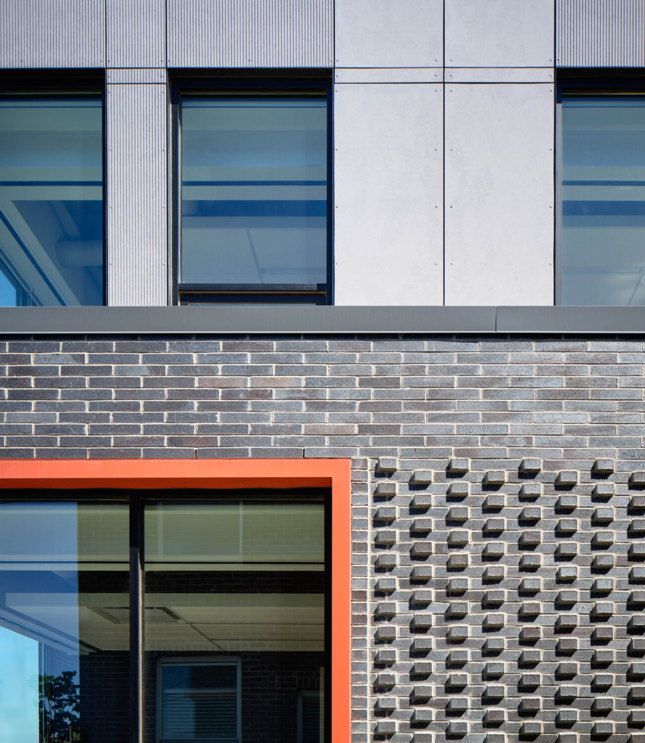 Detail of textured gray panels, patterned dark brick and an orange window surround at Thresholds Center for Mental Wellbeing South