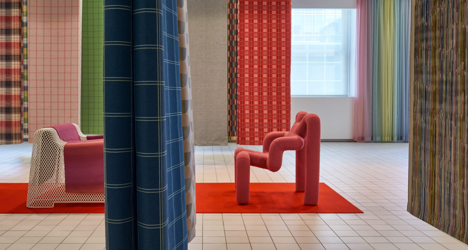 Red sculptural chairs among hanging plaid and striped fabric panels in the Designtex showroom