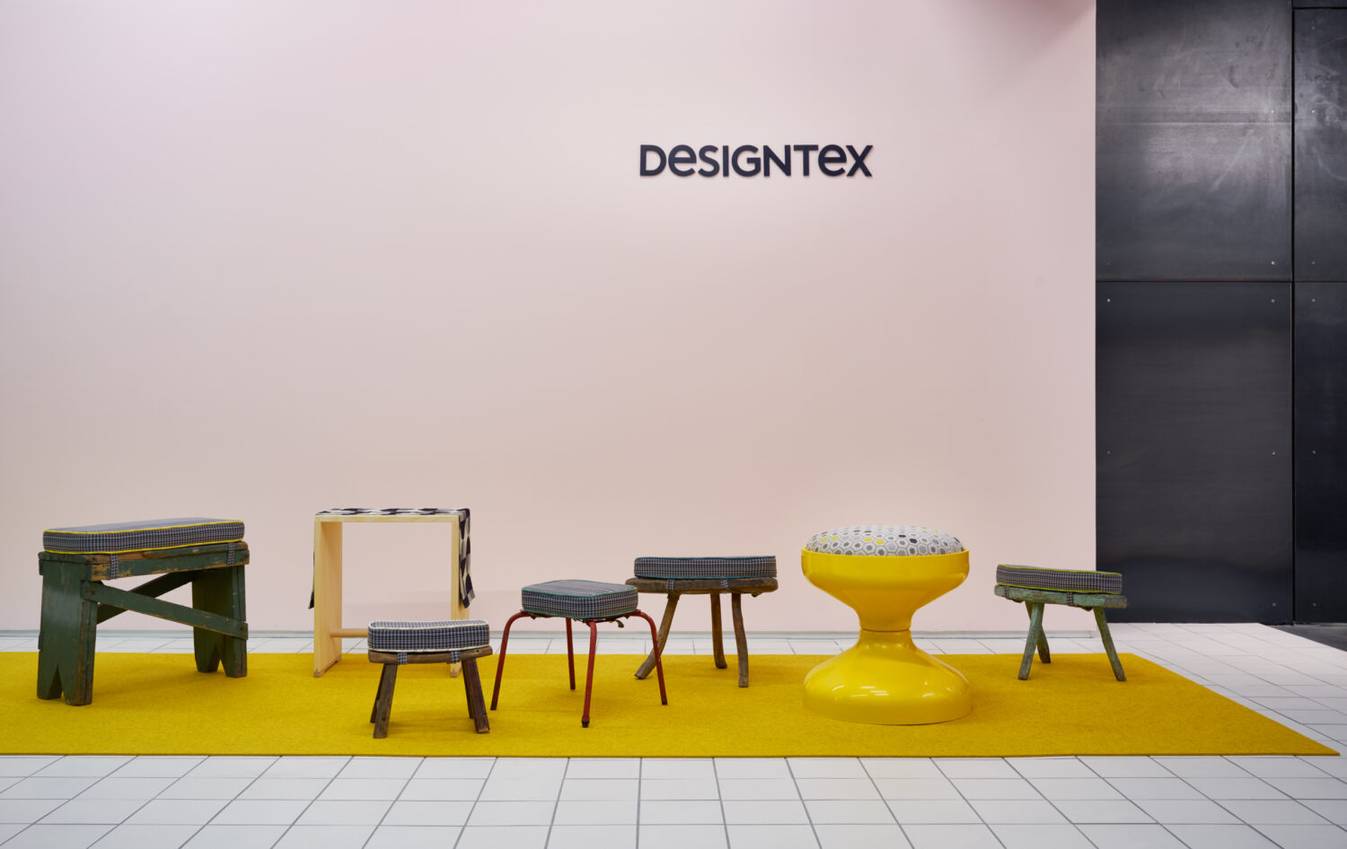 Small stools and side tables on a yellow floor in front of a pale pink wall in the Designtex showroom