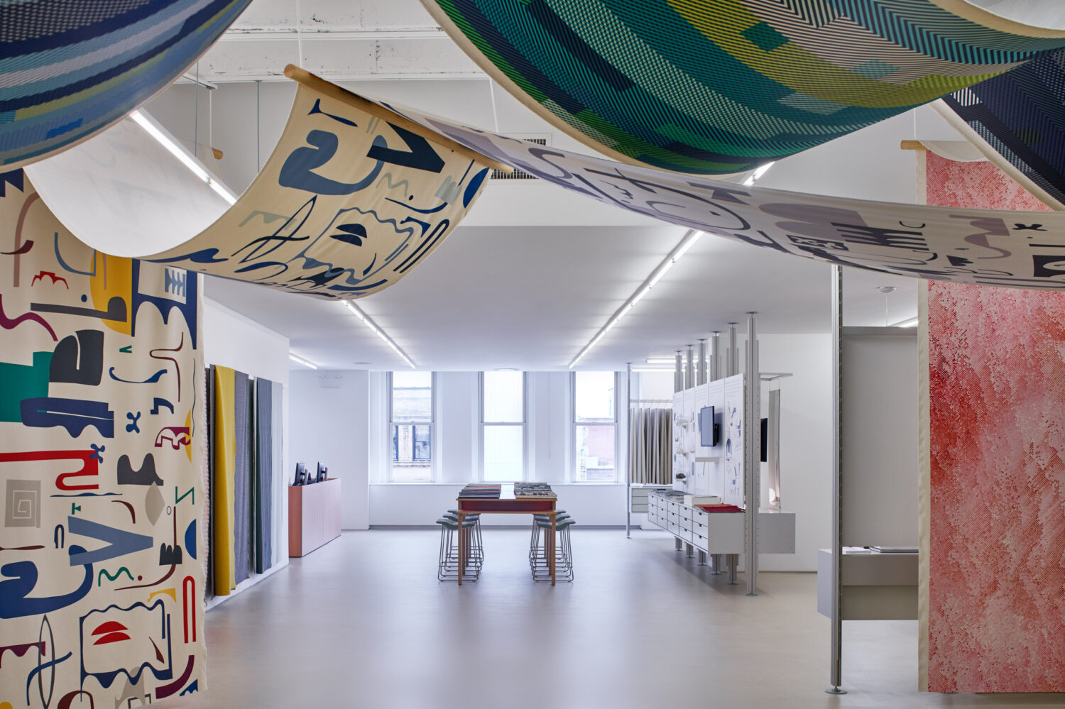 Patterned textiles draped from the ceiling over a bright white Designtex showroom