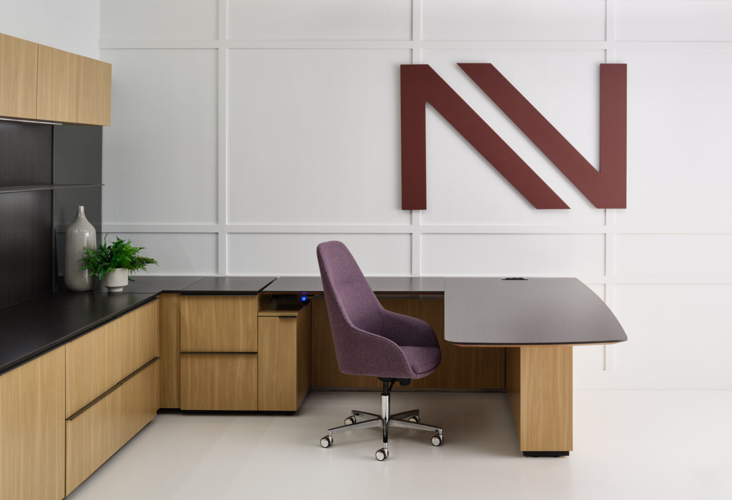 Oak and black desk with a purple task chair below a large burgundy logo in the Enwork showroom