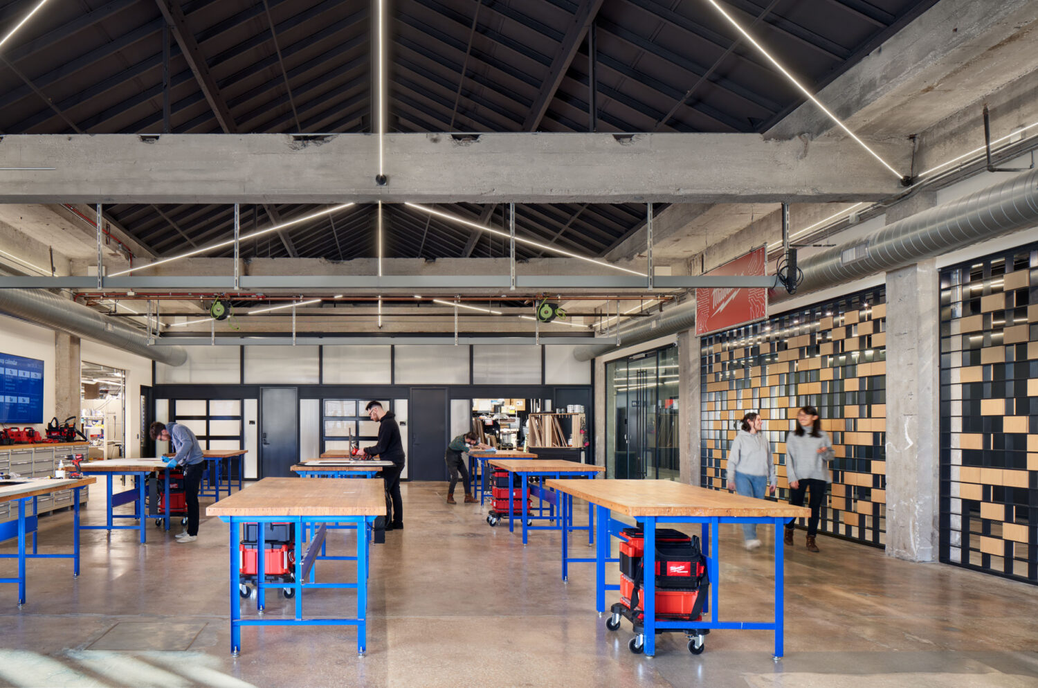Open workshop with blue steel workbenches under exposed timber trusses at mHUB