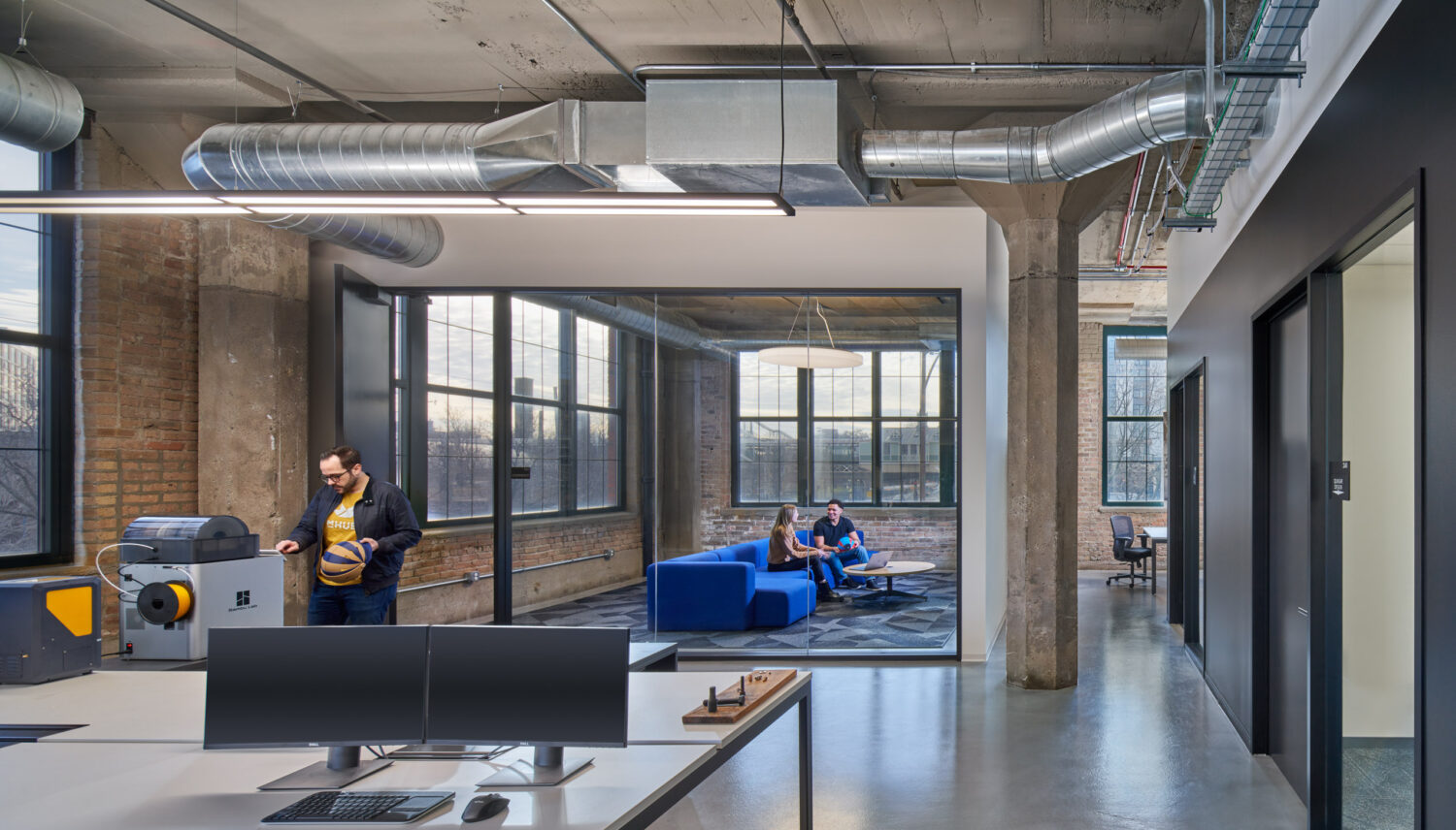Electronics lab workstation with steel windows and a blue lounge beyond at mHUB