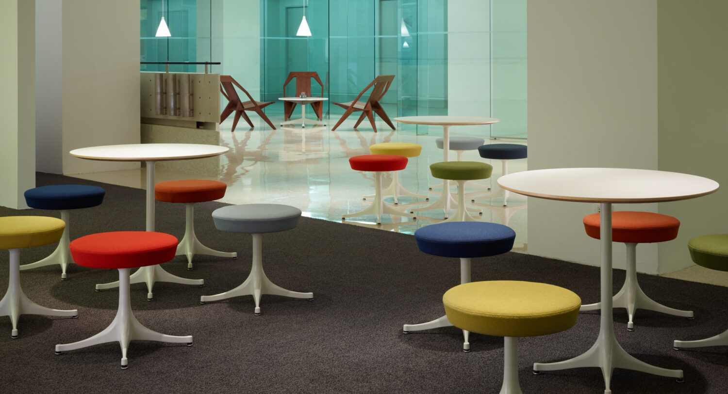 Colorful round stools and white cafe tables on a dark carpet in a Herman Miller showroom