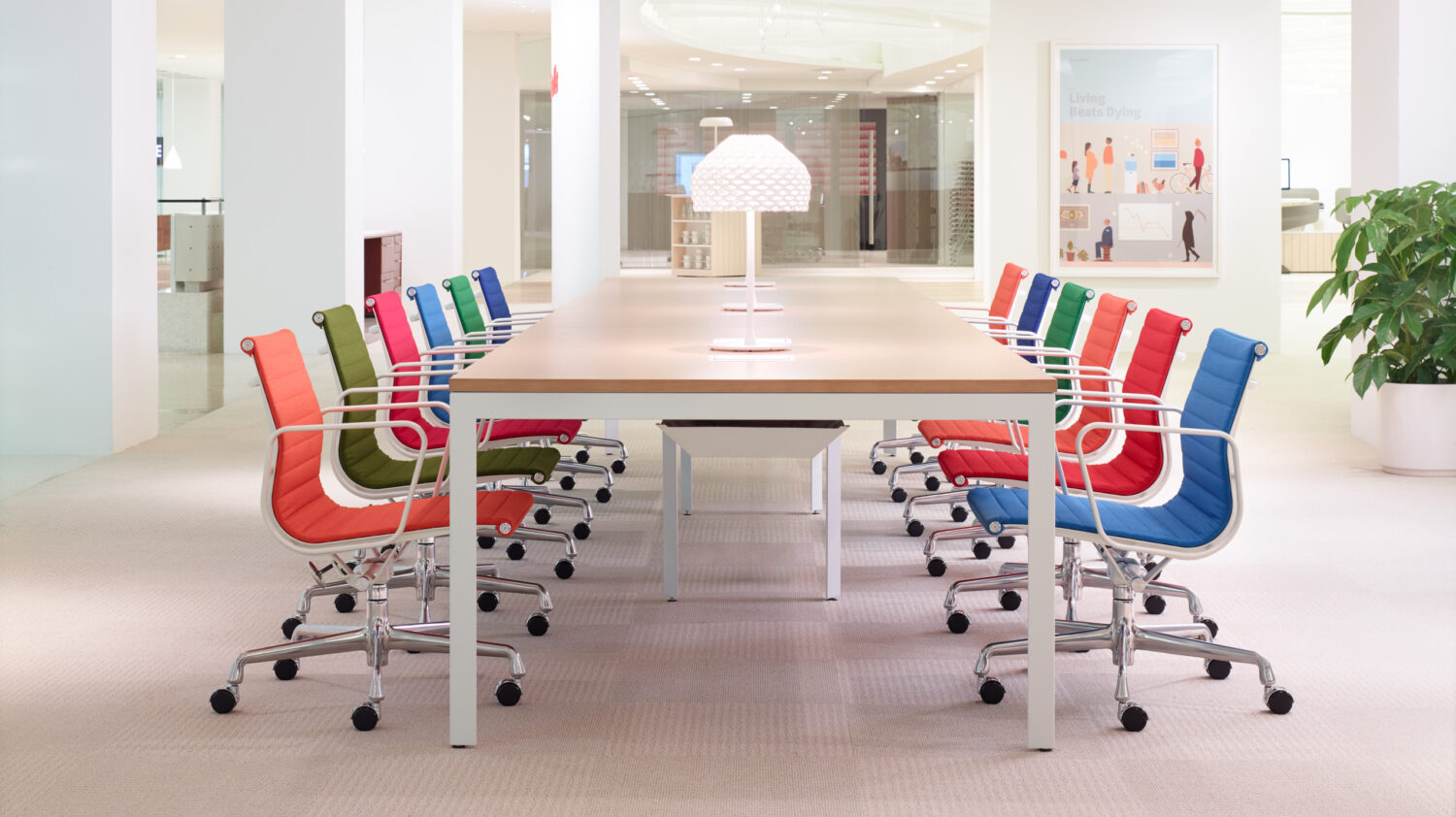 Long conference table lined with red, blue as well as green task chairs in a white Herman Miller showroom