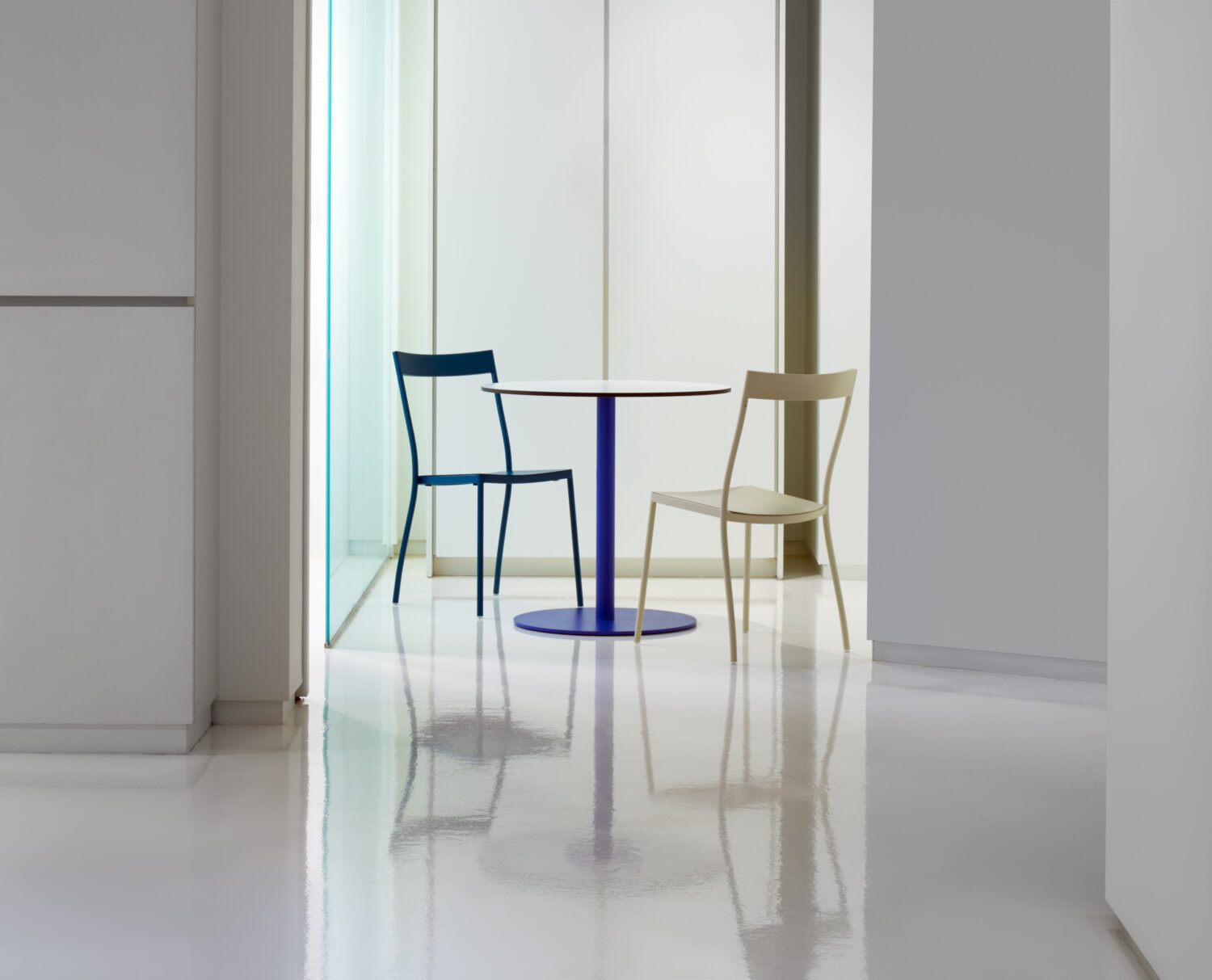 Blue and natural wood cafe chairs at a slim table against white walls in the Keilhauer showroom