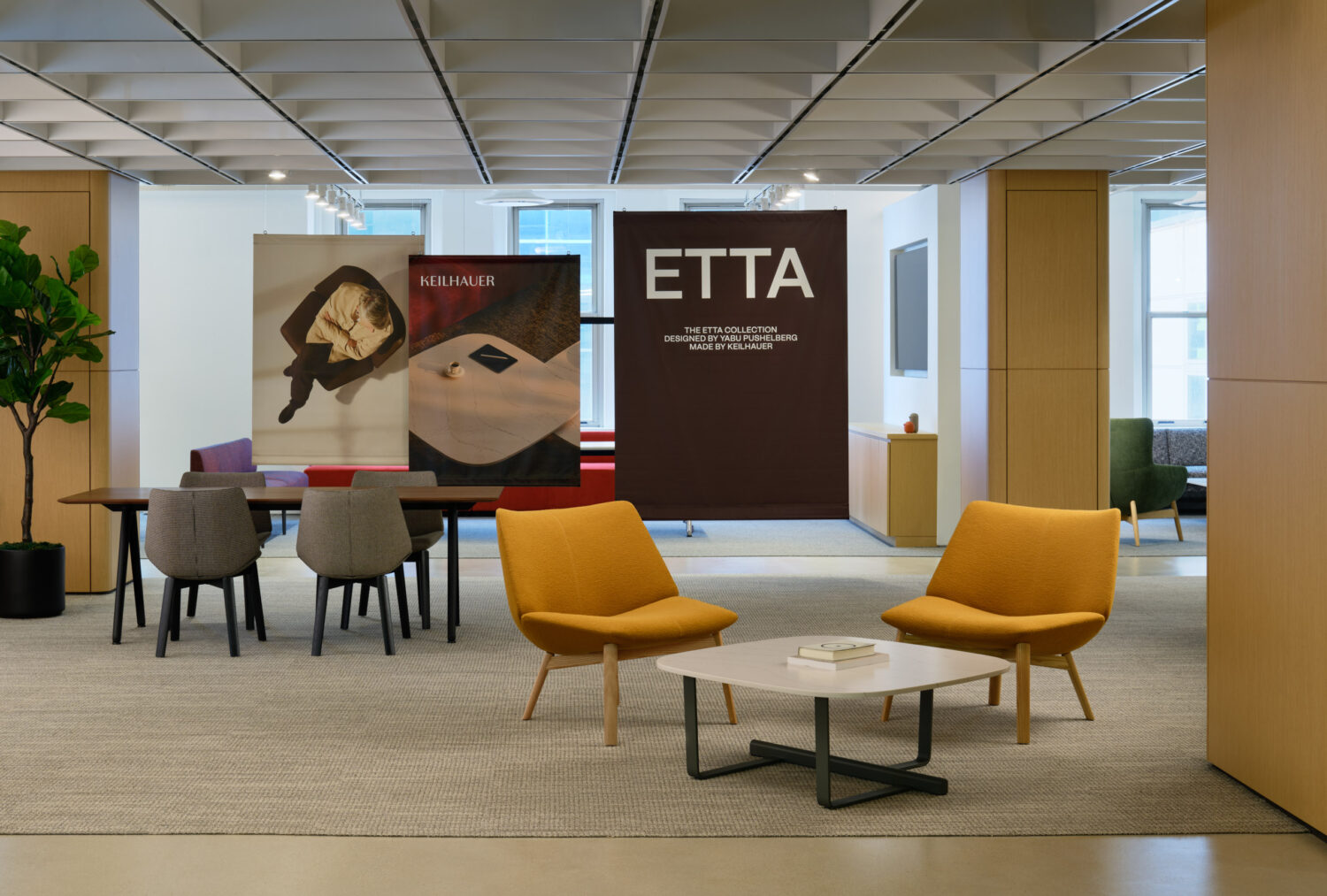 Mustard lounge chairs around a low table beside a dining setting and ETTA graphics in the Keilhauer showroom